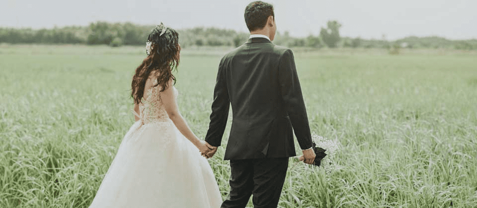 Newlyweds strolling through grassy landscape